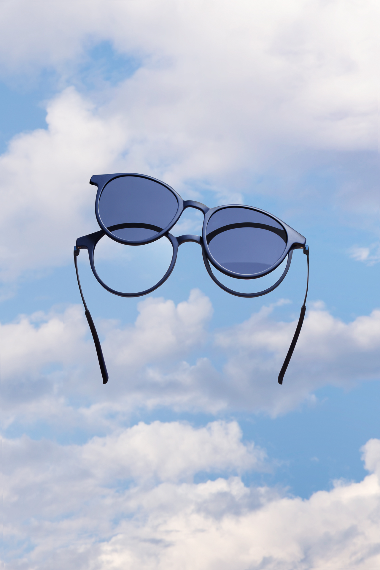 Fotografia creativa di occhiali da sole tondi sospesi tra le nuvole, concept artistico per brand di occhialeria, Belluno.